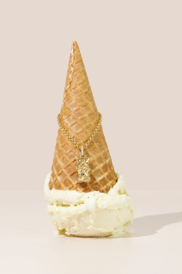 Gold chain and gummy bear pendant wrapped around an Ice cream cone on a beige background