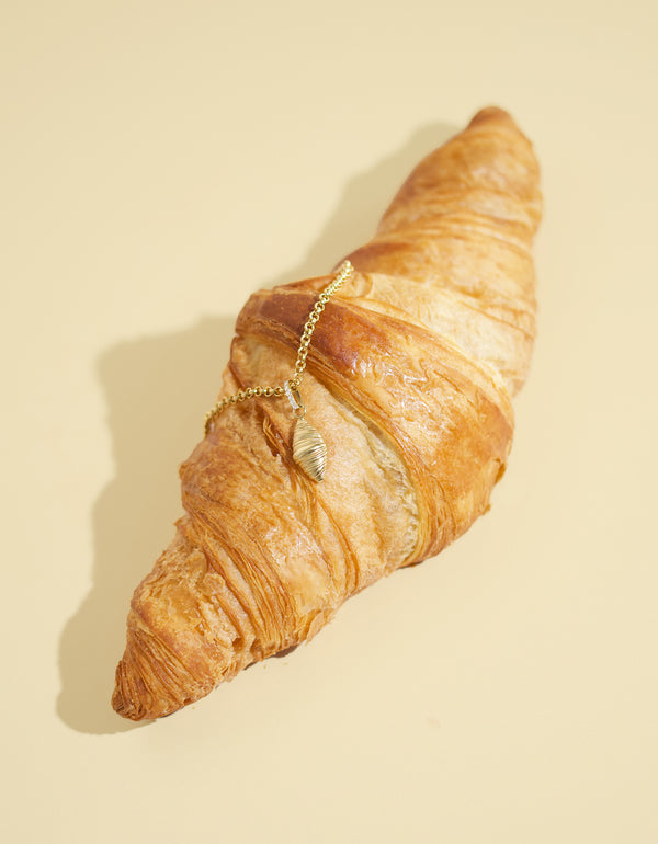 Croissant with a gold chain and croissant pendant on a beige background