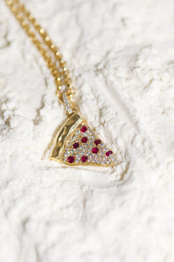 Gold necklace with a pizza slice pendant featuring red gemstones on a bed of white flour